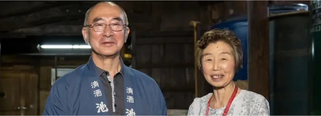 蔵のタンクの前でほほ笑む池嶋 英哲社長と妻の安紀子さん